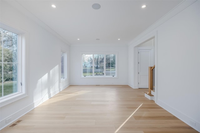 empty room featuring a wealth of natural light, crown molding, and light hardwood / wood-style floors