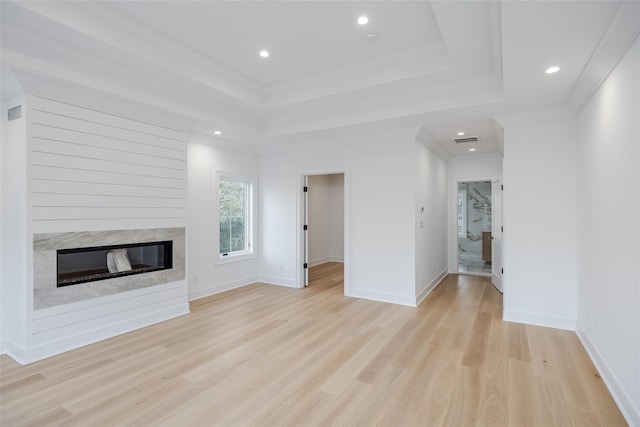 unfurnished living room featuring crown molding, light hardwood / wood-style flooring, a raised ceiling, and a premium fireplace