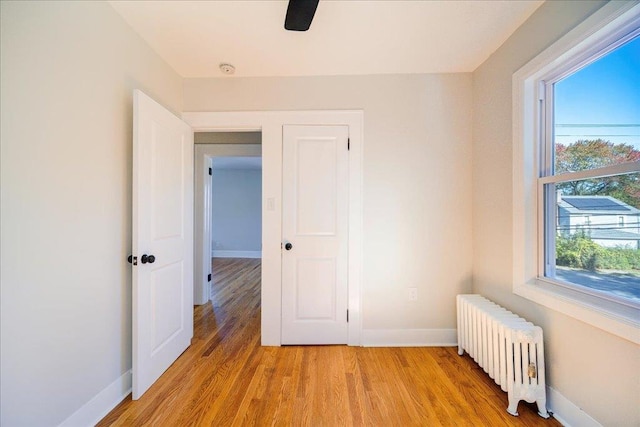 unfurnished bedroom with ceiling fan, light wood-type flooring, radiator, and multiple windows