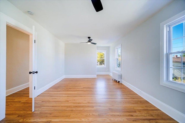 unfurnished room with radiator heating unit, light wood-type flooring, and ceiling fan