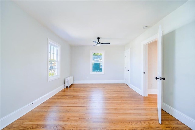 empty room with ceiling fan, a healthy amount of sunlight, light wood-type flooring, and radiator heating unit