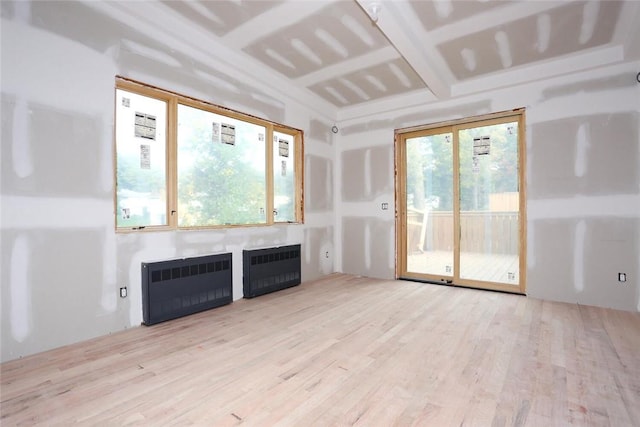 unfurnished living room featuring a healthy amount of sunlight, radiator heating unit, and light hardwood / wood-style flooring