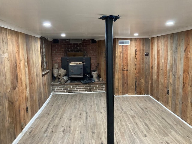 basement with hardwood / wood-style floors, a wood stove, wooden walls, and crown molding