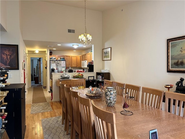 dining space featuring light hardwood / wood-style flooring, a high ceiling, and a notable chandelier