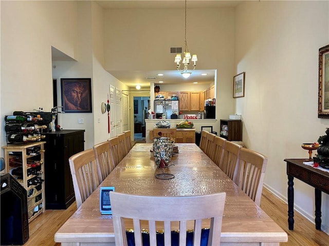 dining space with light hardwood / wood-style flooring, a towering ceiling, and a chandelier