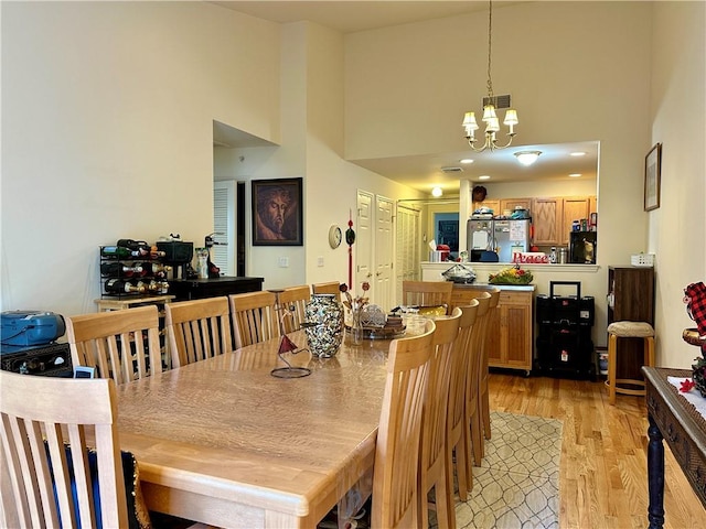 dining space with light hardwood / wood-style floors, a towering ceiling, and an inviting chandelier