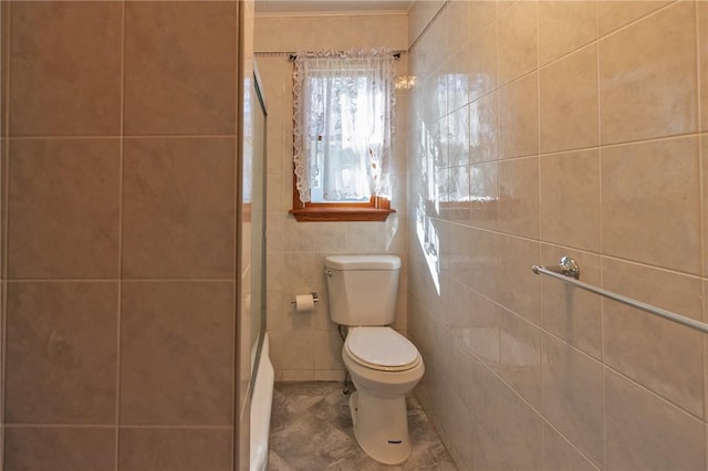 bathroom featuring toilet, a shower with door, and tile walls