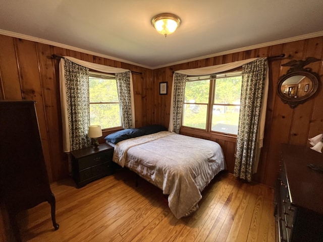 bedroom featuring multiple windows, light hardwood / wood-style flooring, ornamental molding, and wooden walls