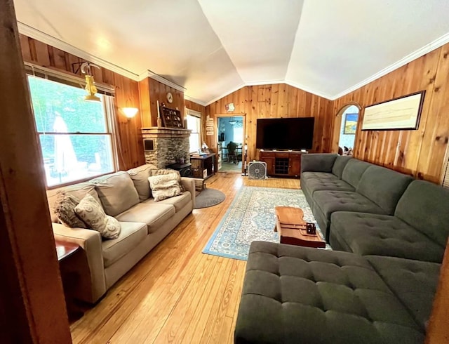 living room featuring hardwood / wood-style floors, crown molding, a stone fireplace, and vaulted ceiling