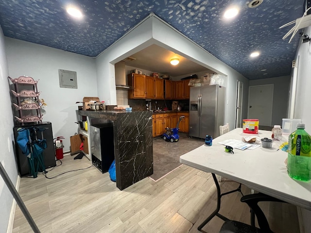 kitchen featuring stainless steel refrigerator with ice dispenser, backsplash, electric panel, kitchen peninsula, and light hardwood / wood-style floors