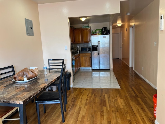 kitchen with electric panel, dark stone countertops, wood-type flooring, and stainless steel refrigerator with ice dispenser