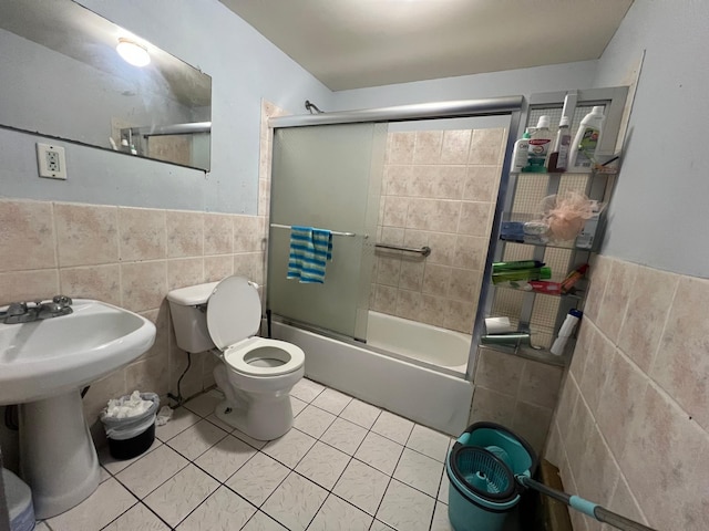 bathroom with tile patterned floors, toilet, tile walls, and combined bath / shower with glass door