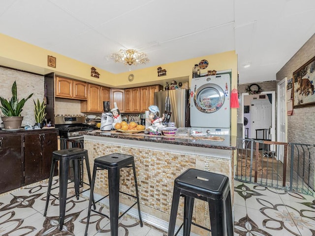 kitchen featuring appliances with stainless steel finishes, a breakfast bar, light tile patterned floors, a notable chandelier, and stacked washer and dryer