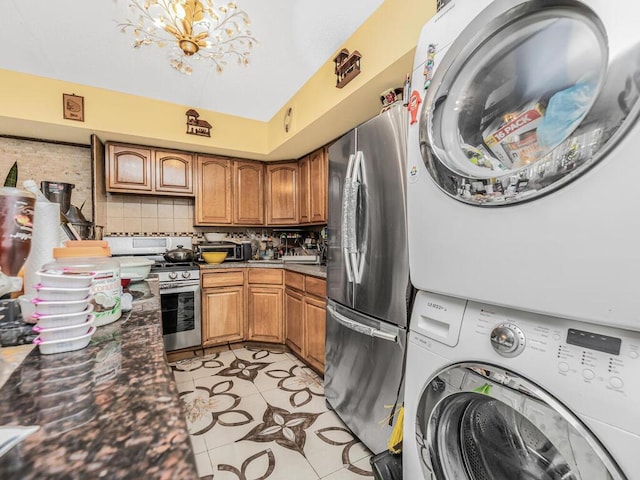 kitchen with decorative backsplash, appliances with stainless steel finishes, light tile patterned floors, a notable chandelier, and stacked washer and dryer