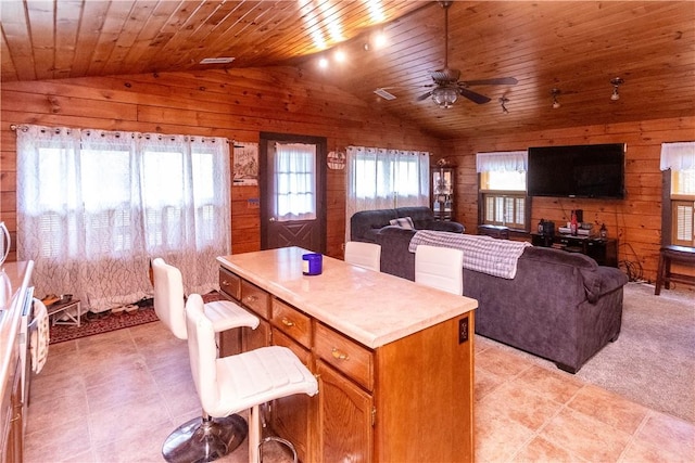 kitchen featuring ceiling fan, a center island, wooden ceiling, wood walls, and lofted ceiling