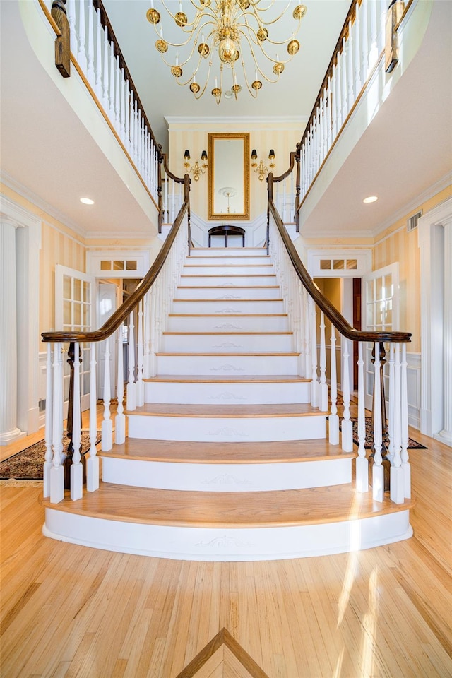 stairway featuring a notable chandelier, wood-type flooring, a towering ceiling, and crown molding