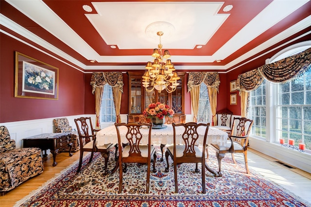 dining area with a tray ceiling, ornamental molding, a notable chandelier, and hardwood / wood-style flooring