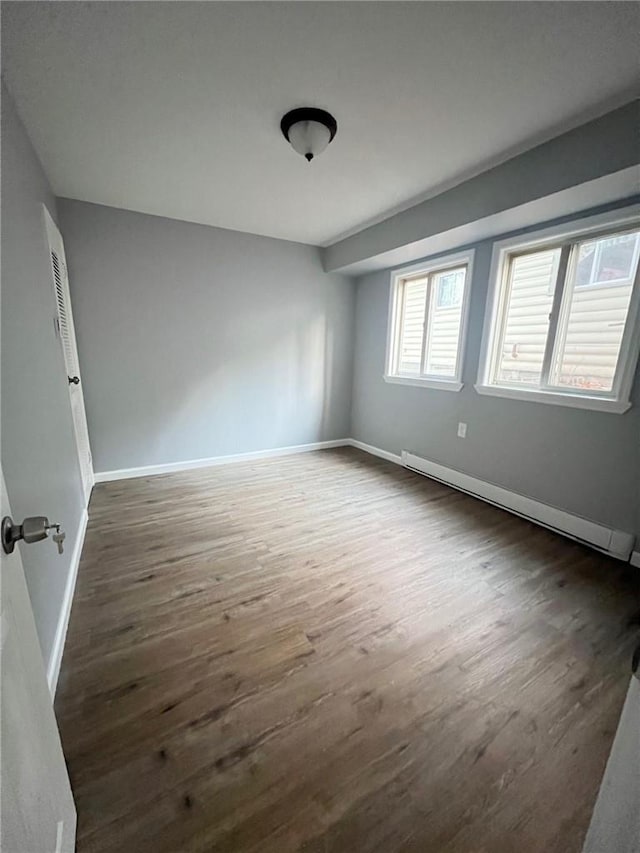 unfurnished room with dark hardwood / wood-style flooring and a baseboard heating unit