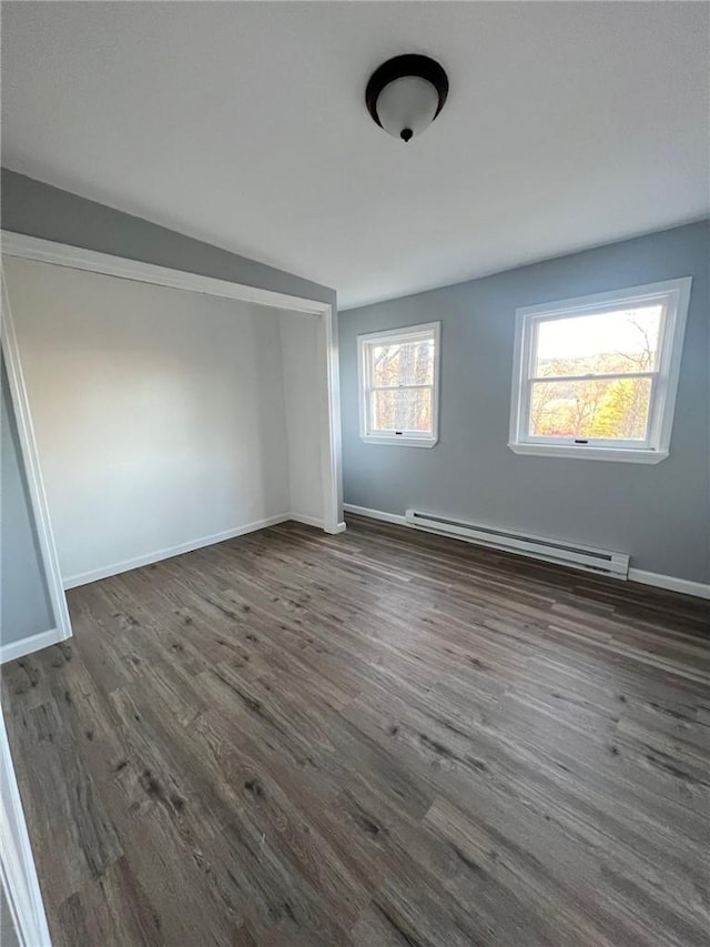 unfurnished room with vaulted ceiling, dark hardwood / wood-style flooring, and a baseboard heating unit