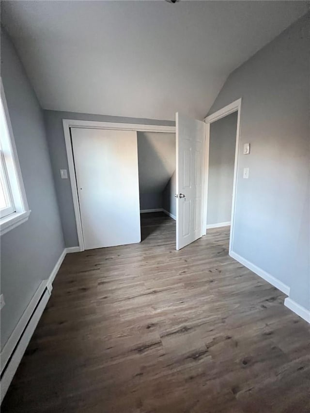 unfurnished bedroom featuring hardwood / wood-style floors, vaulted ceiling, a closet, and a baseboard heating unit