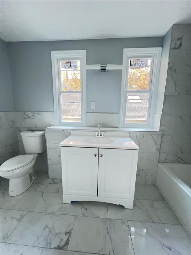 bathroom with a washtub, vanity, tile walls, and toilet