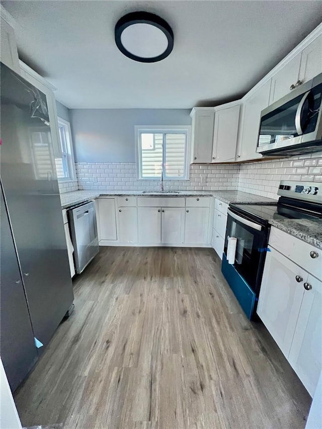 kitchen featuring light stone countertops, white cabinetry, sink, stainless steel appliances, and light hardwood / wood-style floors