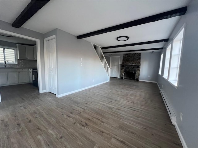 unfurnished living room featuring sink, a fireplace, baseboard heating, beam ceiling, and wood-type flooring