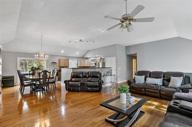 living room featuring lofted ceiling, ceiling fan with notable chandelier, wood finished floors, and baseboards