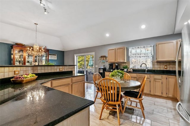 kitchen featuring decorative light fixtures, lofted ceiling, light brown cabinetry, freestanding refrigerator, and a sink