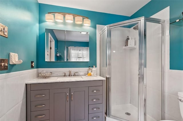 full bathroom featuring a stall shower, toilet, a wainscoted wall, vanity, and tile walls