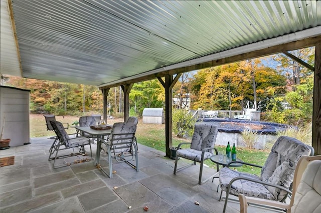 view of patio featuring outdoor dining area, a storage shed, fence, a covered pool, and an outdoor structure