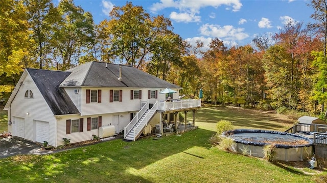 rear view of property featuring a garage, a lawn, a covered pool, stairs, and a deck