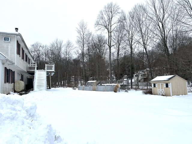 snowy yard with a storage shed, stairway, a deck, and an outbuilding