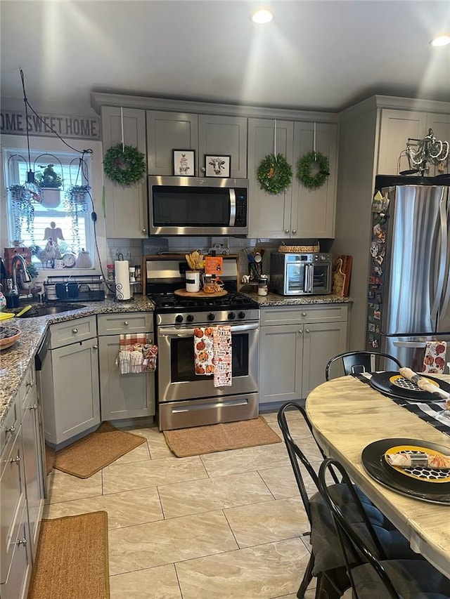 kitchen featuring sink, stainless steel appliances, tasteful backsplash, dark stone countertops, and gray cabinets