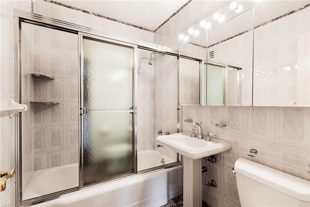 bathroom with toilet, tile walls, and combined bath / shower with glass door