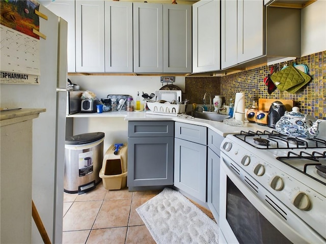 kitchen featuring decorative backsplash, sink, light tile patterned floors, gray cabinets, and white gas stove