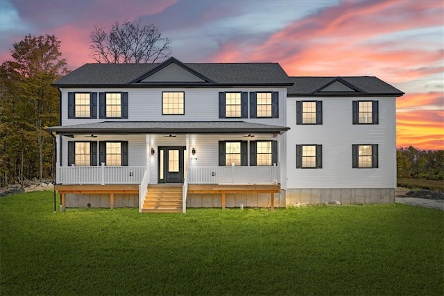 back house at dusk featuring a porch and a yard