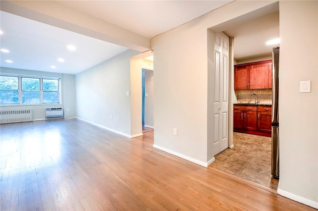 unfurnished living room featuring light hardwood / wood-style floors, radiator, and sink