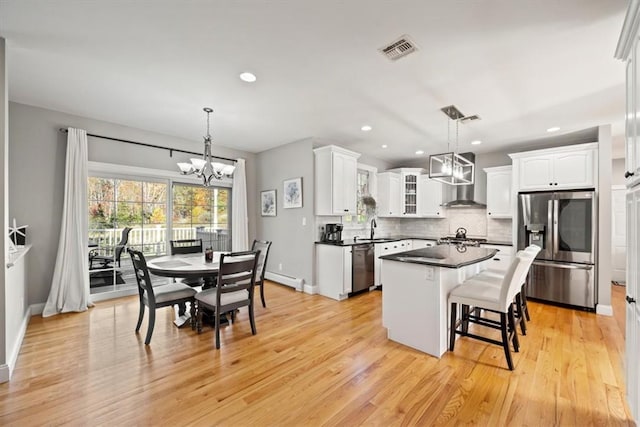 kitchen featuring white cabinets, decorative light fixtures, stainless steel appliances, and light hardwood / wood-style flooring