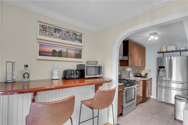 kitchen featuring wall chimney range hood, crown molding, decorative backsplash, appliances with stainless steel finishes, and radiator heating unit