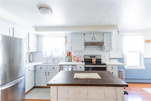 kitchen featuring a baseboard heating unit, stainless steel appliances, tasteful backsplash, a kitchen island, and sink