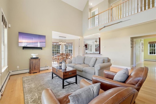 living room with a wealth of natural light, high vaulted ceiling, light hardwood / wood-style floors, and ceiling fan with notable chandelier