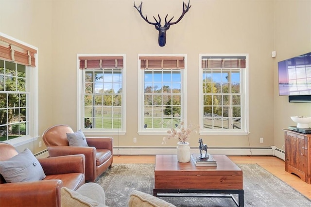 interior space with a wealth of natural light, a notable chandelier, a baseboard heating unit, and light wood-type flooring