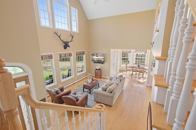 living room with light wood-type flooring, high vaulted ceiling, and a baseboard heating unit