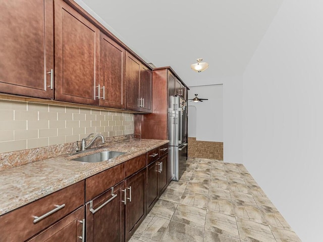 kitchen with light stone countertops, decorative backsplash, stainless steel fridge, ceiling fan, and sink