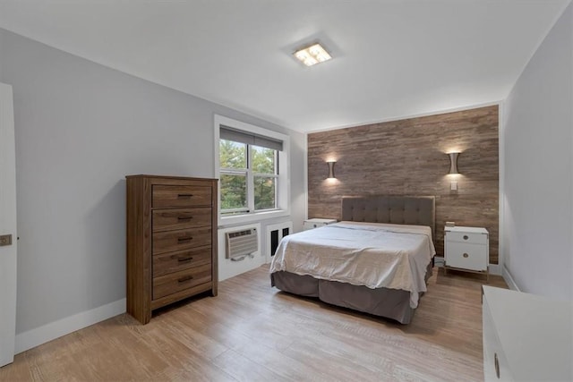 bedroom featuring a wall unit AC, wooden walls, and light hardwood / wood-style flooring