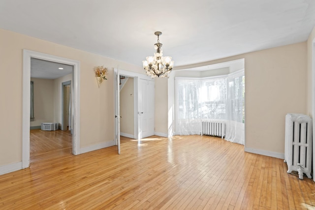 empty room with an inviting chandelier, light hardwood / wood-style flooring, and radiator