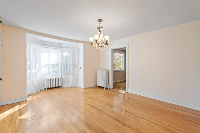 unfurnished room with light wood-type flooring, radiator heating unit, and a chandelier