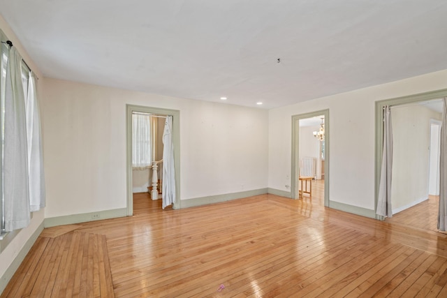 spare room with a chandelier, radiator heating unit, and light hardwood / wood-style flooring