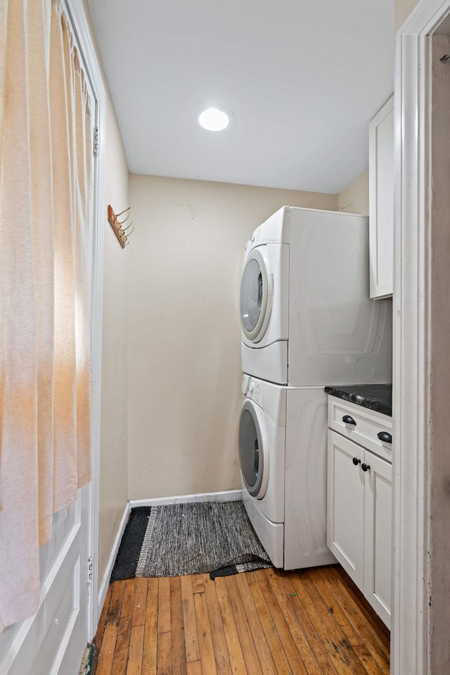 laundry area featuring cabinets, stacked washing maching and dryer, and dark hardwood / wood-style floors